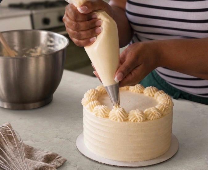 Baker piping buttercream onto a fresh cake